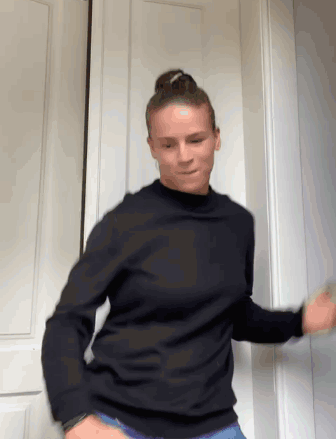 A Woman Wearing A Black Sweater Is Dancing In Front Of A Door GIF