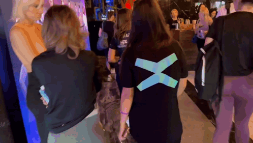 A Woman Wearing A Black T-Shirt With A Blue X On The Back GIF
