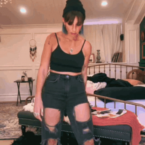 A Woman Wearing A Black Tank Top And Ripped Jeans GIF