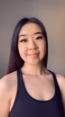 A Woman Wearing A Black Tank Top Is Smiling For The Camera GIF