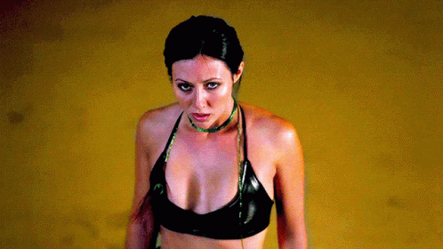A Woman Wearing A Black Top And A Green Necklace GIF