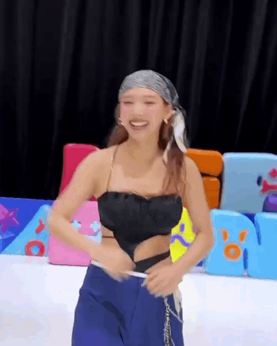 A Woman Wearing A Black Top And Blue Pants Is Standing In Front Of A Playground . GIF