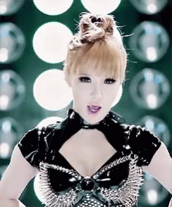 A Woman Wearing A Black Top With Spikes On It Is Standing In Front Of A Bunch Of Lights . GIF