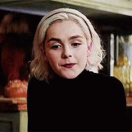 A Woman Wearing A Black Turtleneck And A Headband Looks At The Camera GIF
