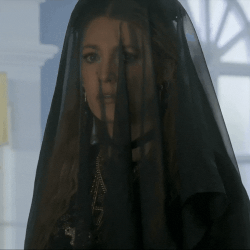 A Woman Wearing A Black Veil Is Standing In Front Of A Window GIF
