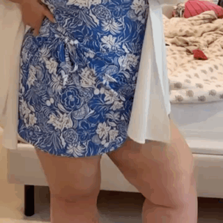 A Woman Wearing A Blue And White Floral Dress Is Standing In Front Of A Bed . GIF