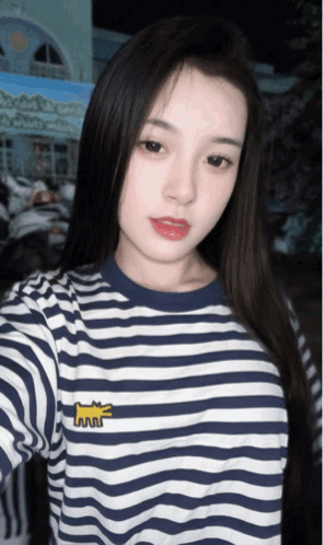 A Woman Wearing A Blue And White Striped Shirt Takes A Selfie With Her Phone GIF