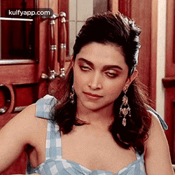 A Woman Wearing A Blue Dress And Earrings Is Sitting In Front Of A Door . GIF
