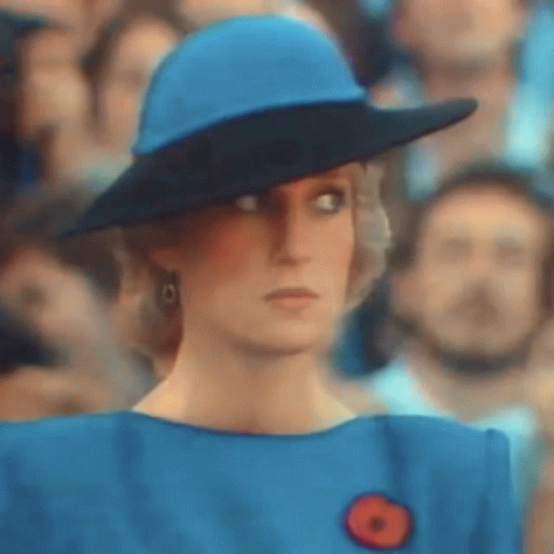 A Woman Wearing A Blue Hat And A Blue Dress Is Standing In Front Of A Crowd Of People . GIF
