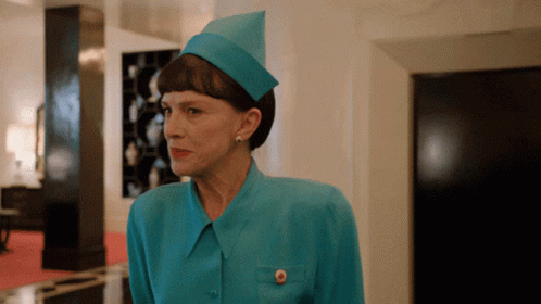 A Woman Wearing A Blue Hat And A Blue Shirt Has A Gold Button On Her Pocket GIF