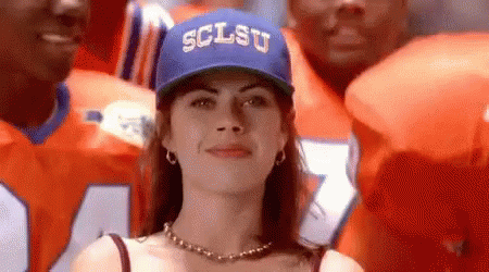 A Woman Wearing A Blue Hat With The Word Sclsu On It Is Standing In Front Of A Football Team . GIF