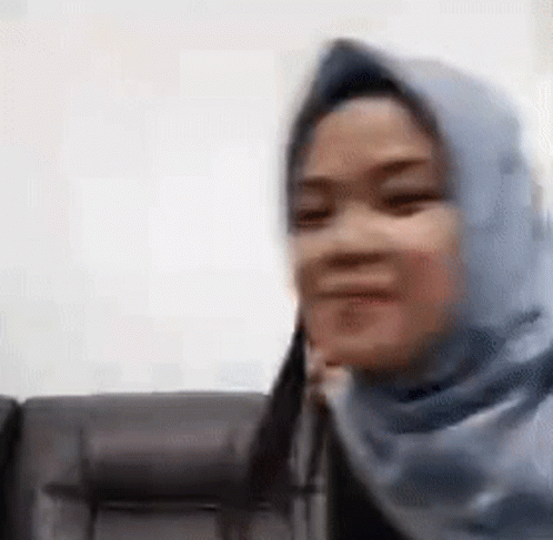 a woman wearing a blue hijab is sitting on a couch and smiling .