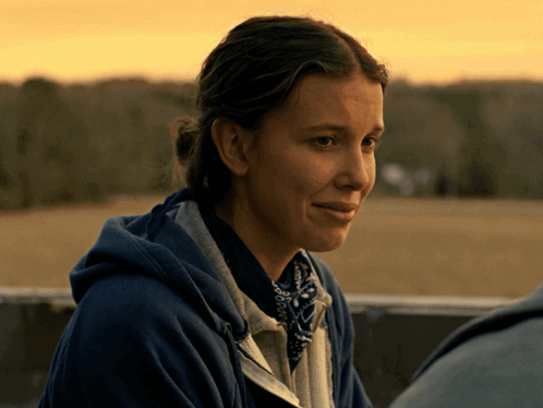 A Woman Wearing A Blue Hoodie And A Bandana Looks Down GIF