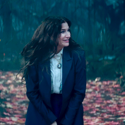 A Woman Wearing A Blue Jacket And White Shirt Is Standing In A Forest . GIF