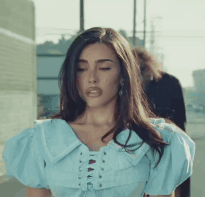 A Woman Wearing A Blue Lace Up Top Is Standing On A Sidewalk . GIF