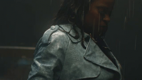A Woman Wearing A Blue Leather Jacket Is Standing In The Rain GIF