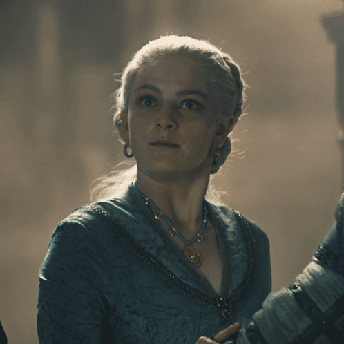A Woman Wearing A Blue Necklace And Earrings Looks At The Camera GIF