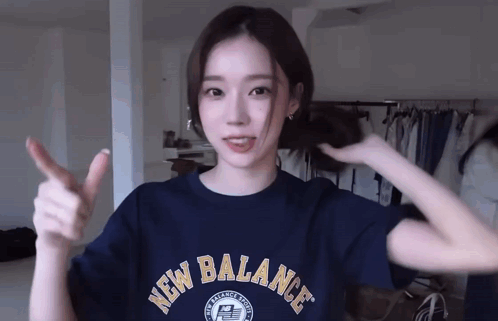 A Woman Wearing A Blue New Balance Shirt Is Giving A Thumbs Up . GIF
