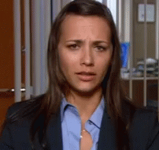 A Woman Wearing A Blue Shirt And A Suit Is Making A Sad Face . GIF