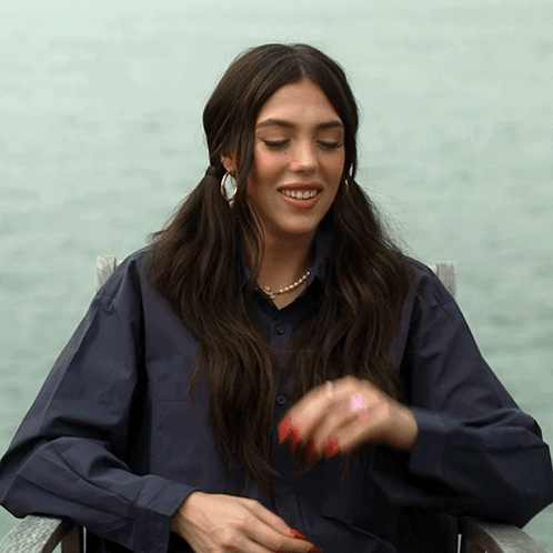 A Woman Wearing A Blue Shirt And Pearls Is Sitting In A Chair GIF