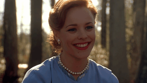 A Woman Wearing A Blue Shirt And Pearls Smiles For The Camera GIF