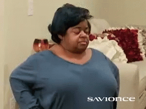 A Woman Wearing A Blue Shirt Is Standing In Front Of A Couch With The Words Savionce On The Bottom GIF