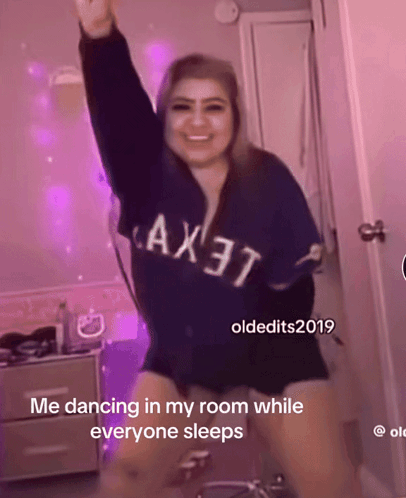 a woman wearing a blue shirt that says ax37 is dancing in a room while everyone sleeps