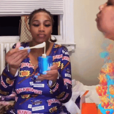 A Woman Wearing A Blue Shirt That Says Backwoods On It Is Eating Something GIF
