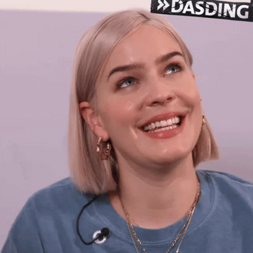 A Woman Wearing A Blue Shirt With A Microphone Around Her Neck Smiles GIF