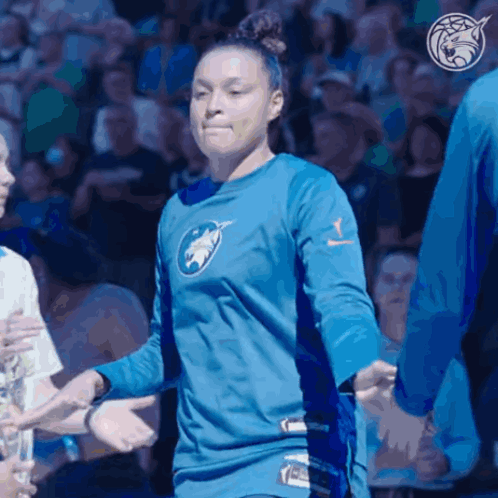 A Woman Wearing A Blue Shirt With A Wolf On It Shakes Hands With Other People GIF