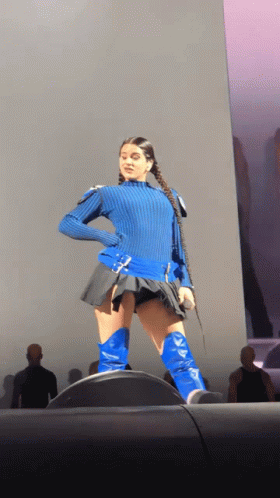 A Woman Wearing A Blue Sweater And Blue Boots Is Standing On A Stage GIF