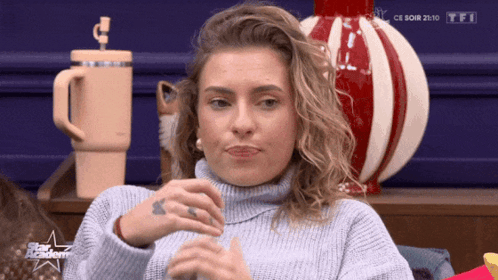 Woman In Blue Sweater Sitting In Front Of TFI Logo GIF