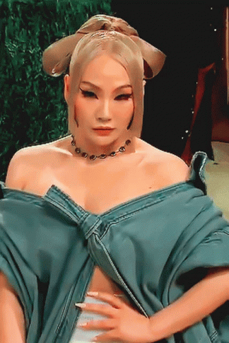 A Woman Wearing A Blue Top And A Necklace Is Looking At The Camera GIF