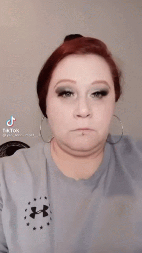 A Woman Wearing A Blue Under Armour Shirt Is Applying Makeup To Her Eye . GIF