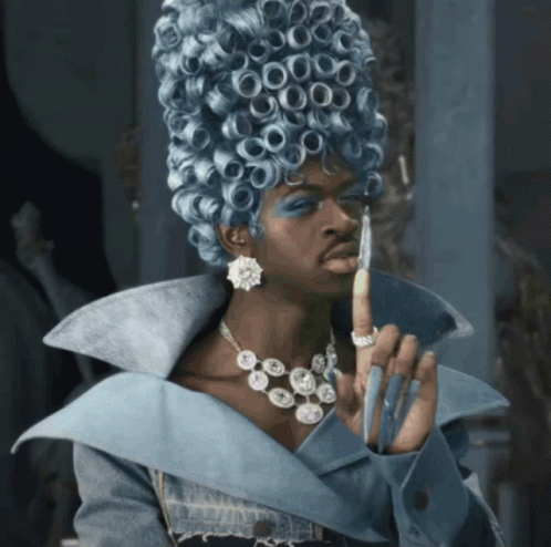 A Woman Wearing A Blue Wig And A Necklace Holds Her Finger Up GIF