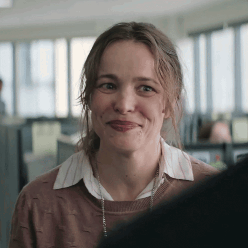 a woman wearing a brown sweater and a white shirt smiles for the camera
