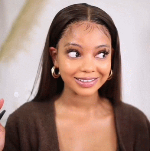 A Woman Wearing A Brown Sweater And Hoop Earrings Is Smiling And Looking To The Side . GIF
