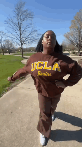 a woman wearing a brown ucla bruins sweatshirt is walking down a sidewalk .