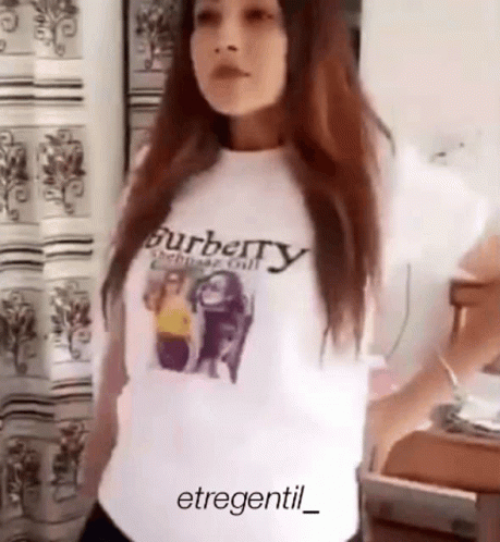 a woman wearing a burberry t-shirt is standing in front of a window .