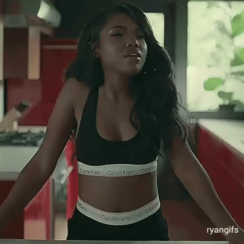 A Woman Wearing A Calvin Klein Bra And Shorts Is Standing In A Kitchen . GIF