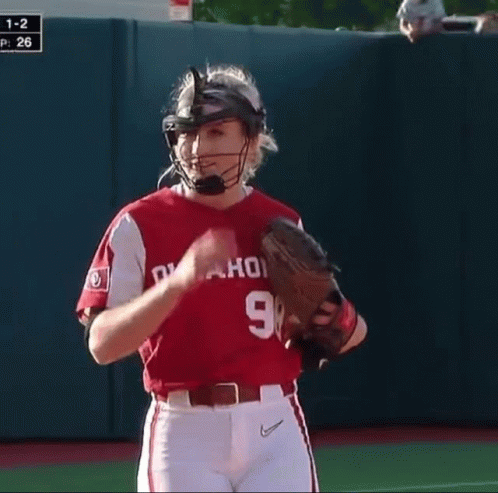 a woman wearing a catcher 's helmet and glove stands on the field