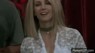 A Woman Wearing A Choker And A White Shirt Is Smiling While Sitting In A Theatre . GIF