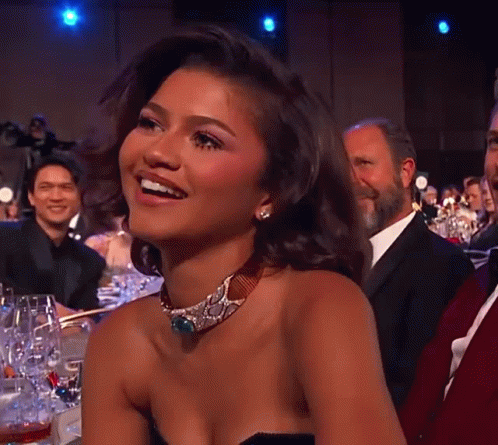A Woman Wearing A Choker Is Smiling In Front Of A Crowd Of People GIF