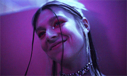 A Woman Wearing A Choker Is Smiling In Front Of A Purple Wall GIF