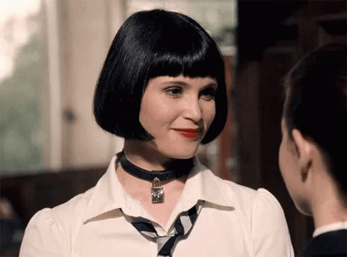 A Woman Wearing A Choker Necklace And A White Shirt Looks At Another Woman GIF