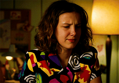 A Woman Wearing A Colorful Shirt Is Sitting In A Dark Room GIF