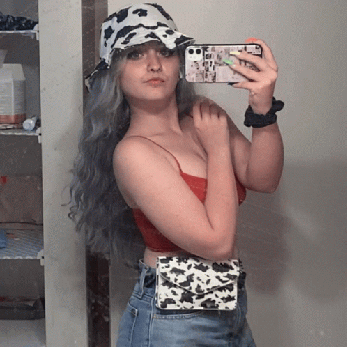A Woman Wearing A Cow Print Hat Takes A Selfie With Her Phone GIF