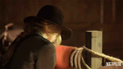 A Woman Wearing A Cowboy Hat Is Standing Next To A Netflix Logo GIF