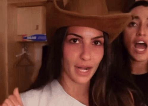a woman wearing a cowboy hat is standing next to another woman wearing a white shirt .