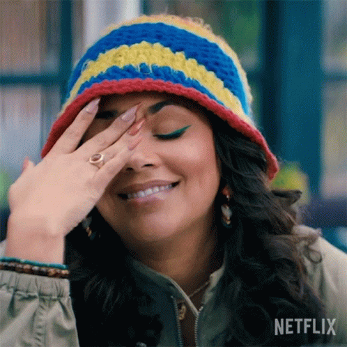 A Woman Wearing A Crocheted Hat And A Ring Is Smiling And Covering Her Face With Her Hand . GIF